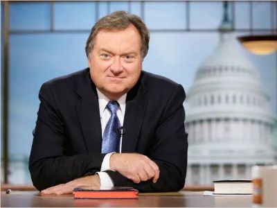 Tim Russert is sitting on a desk with folded hands.